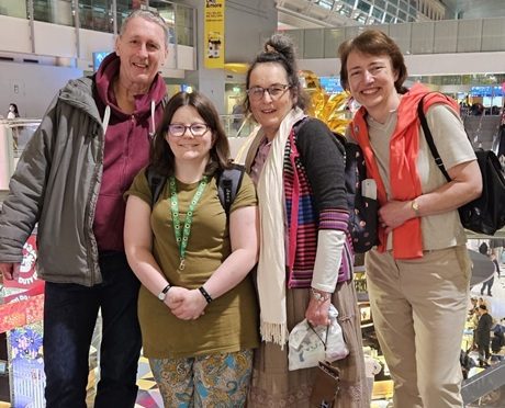 Four people (3 women, 1 man) stand close together and smile for the camera in a bustling airport on their way to India for a Roofbreaker trip (2024)