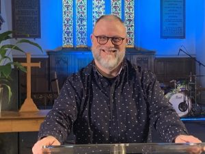 Revd Neil Robinson with a stained glass window in the background