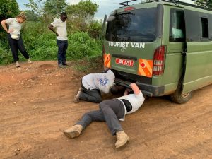 Two members of the team work on the van, crawling under the back, while another team member watches