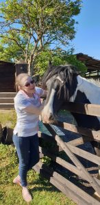 Minna Moffat-Feldman who is Deaf - she is pictured smiling and stroking a horse next to a gate