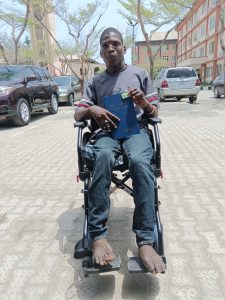 A young Nigerian man sat in a wheelchair, smiling, holding a Bible