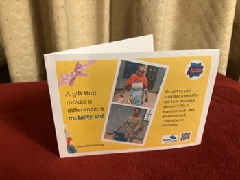 Photo of a printed gift card on a yellow background, with text on the left that says: 'A gift that makes a difference: a mobility aid' To the right are two photos of disabled women in Rwanda: one a young woman using shiny aluminium crutches; one an older woman pushing a wheeled walking frame. On the right is some text saying: 'My gift to you supplies a mobility aid so a disabled person's life is transformed - like Jannette and Didancien in Rwanda'. There are logos for Through the Roof www.throughtheroof.org and their project Wheels for the World. There is also a QR code linking to their International Missions page at https://throughtheroof.org/international-mission/