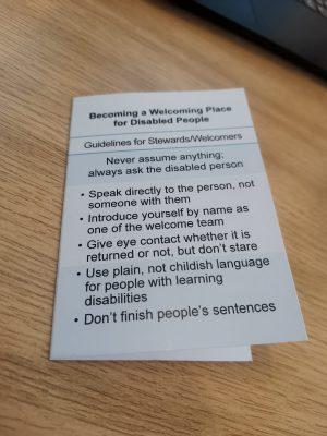 Front of a pocket-sized white and blue card with heading 'Becoming a Welcoming Place for Disabled People: Guidelines for Stewards/Welcomers'. Text below gives advice, e.g. 'Never assume anything; always ask the disabled person'.