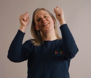 Close up of a smiling woman doing the Makaton sign for 'good' (a double 'thumbs up')