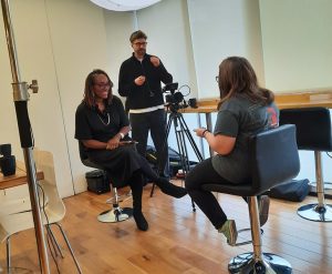 Video filming in a studio: two women having an interview while a cameraman records them.