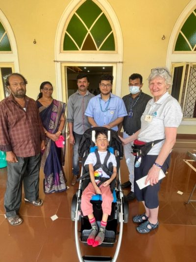 Joann,  a young boy, sits in his newly fitted mobility buggy. He's surrounded by members of his family, plus staff from the Indian hospital, and one member of the Wheels for the World team