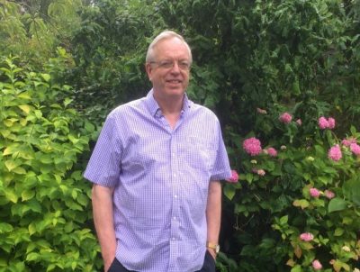 Jonathan Edwards, a speaker at one of our events, standing in a garden in front of some bright pink plants.