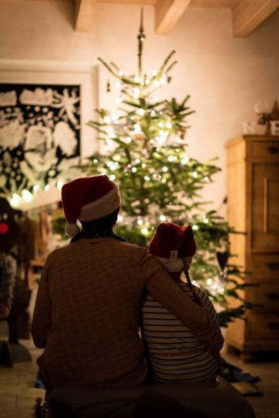 a parent and child in santa hats sitting in front of a lit christmas tree