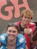Two young UK volunteers on a boat trip: a man in a red life jacket and a woman in a blue life jacket.