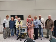 A group photo of about 10 UK volunteers at an airport, with luggage and trolleys.