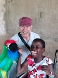 A young Ugandan girl in a wheelchair, laughing at a parrot puppet, held by a male UK volunteer.