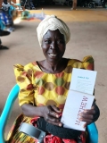 Ugandan lady in yellow dress holding Gospel and some crutches.