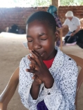 A young Ugandan girl sat in a chair with hands together and eyes closed in prayer