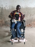 A young Ugandan man, sat smiling in a wheelchair, holding a Bible.