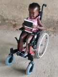 A little Ugandan girl sat in a wheelchair holding a Bible.