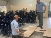 Two men in grey Wheels for the World T shirts, working on constructing something from planks of plywood. 