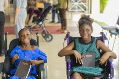 Two smiling children in wheelchairs smiling broadly and holding Bibles. 