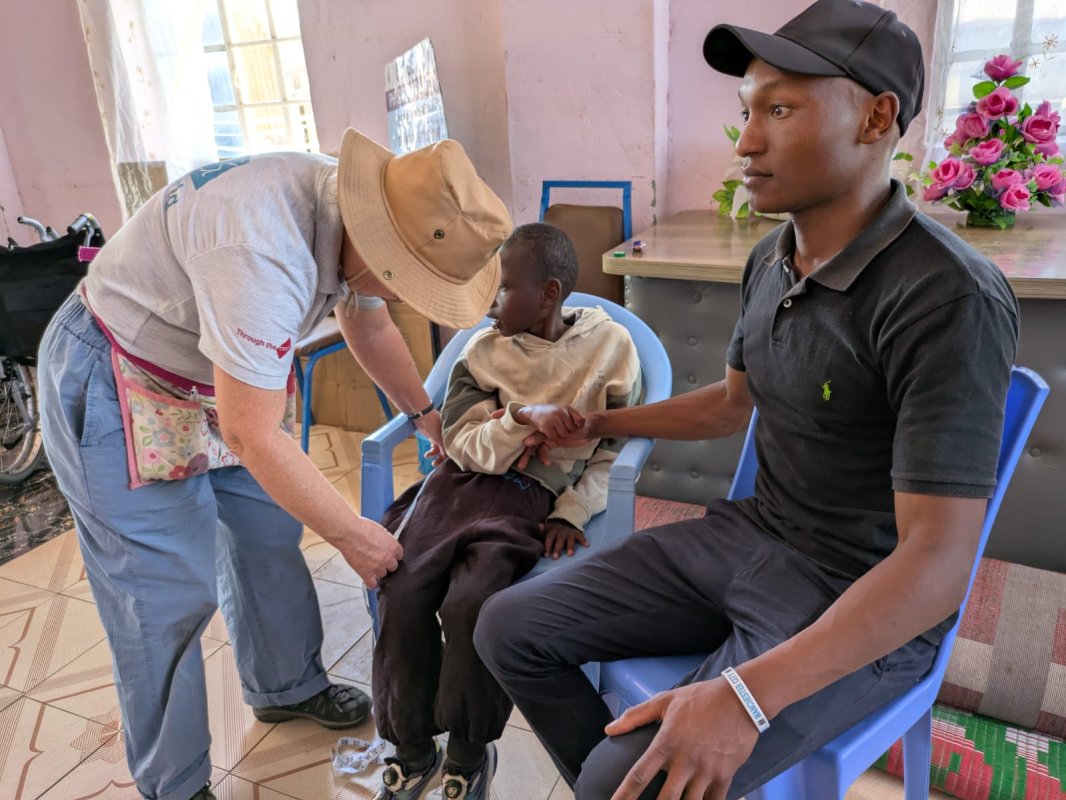 Helen, a UK volunteer, measuring a child's limbs to choose a suitable wheelchair. The child's father sits beside her.