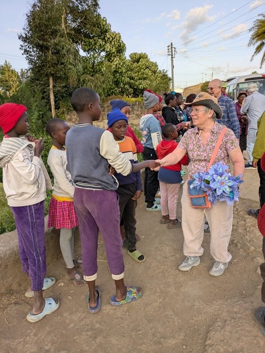 A group of Kenyan women and children welcome the UK mission team, and present a UK volunteer (Helen) with flowers.