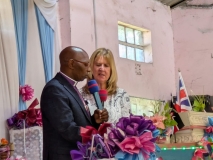 Kathy, a fair haired female UK volunteer, and Pastor Davis, a Kenyan minister wearing glasses: speaking at the front of a Church