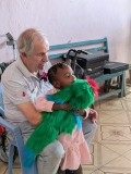 Neil, a grey-haired male volunteer, shows a green parrot puppet to a child in Kenya