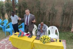Trevor, a British member of the Churches Inclusion team, talking to the crowd from behind a yellow cloth-covered table.