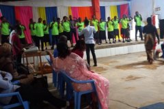 A group of people all in the same yellow-green tshirt singing together on the stage