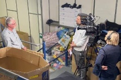 Shaun, our missions manager, is interviewed by a camera crew, he's standing in our wheelchair warehouse, surrounded by bits of gear that are being repaired to send overseas