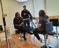 Video filming in a studio: two women having an interview while a cameraman records them.