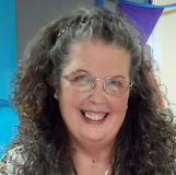 Pat-Eyres-portrait_Smiling middle-aged woman with long, curly, brown hair and glasses 