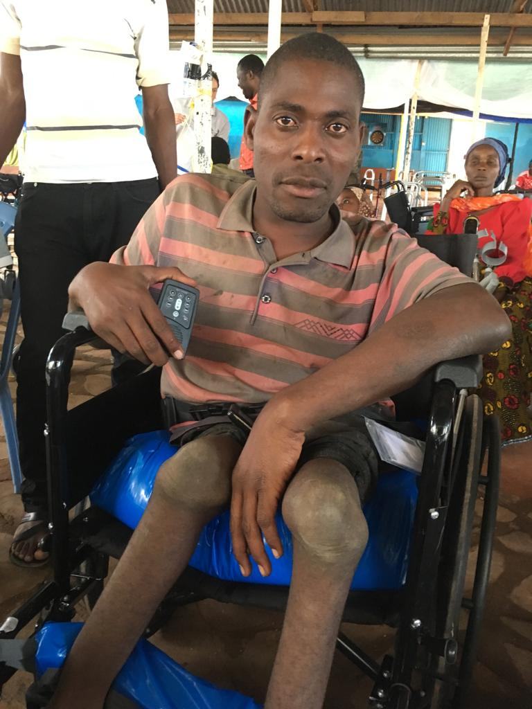 A man in a striped t-shirt sits in his new wheelchair