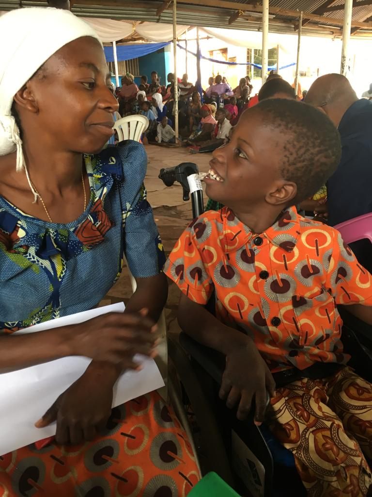 A mum and son smiling at each other as he sits in his new wheelchair