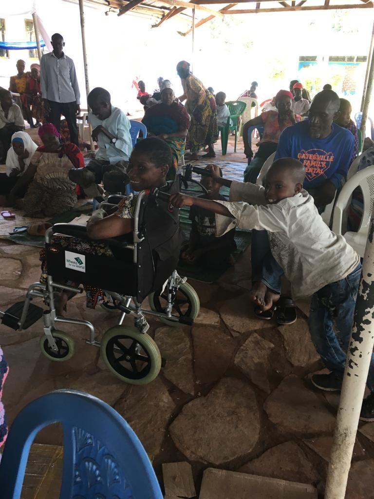 A lady in a new wheelchair is pushed along by a smiling child