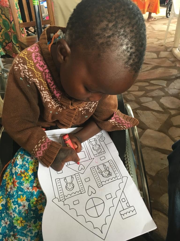 Feis, a young girl, sits and draws on a colouring sheet in her wheelchair