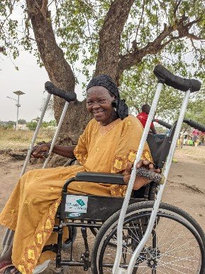 Ester sits in her new wheelchair, with her crutches on either side of her