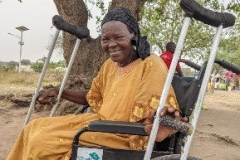 Ester sits in her new wheelchair, with her crutches on either side of her