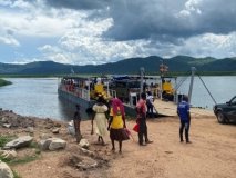 A small ferry boat sat waiting on a lake , with a group of local people standing by the boat